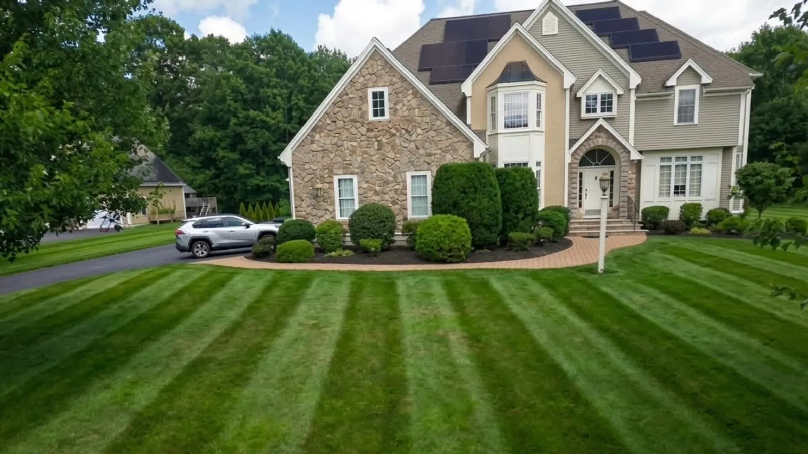 Freshly mowed striped lawn and trimmed shrubs at a stone-front colonial home in MetroWest, MA, maintained by Procopio Landscaping